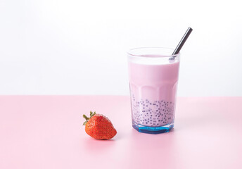 strawberry milk bubble tea in a glass with a straw and strawberry berry on a pink background