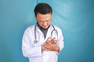 A portrait of a young Asian male doctor looks in pain on his chest