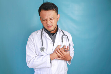 A portrait of a young Asian male doctor looks in pain on his chest