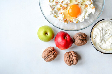 Ingredients for dessert: apples, walnuts, cottage cheese with a broken egg and raisins in a bowl, sour cream with semolina, top view