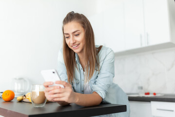 Lovely young woman using smartphone in the kitchen