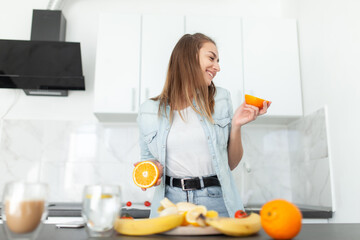 Cheerful young woman having fun with orange slices in the kitchen. Healthy food. Energy Boost, Vitamin C