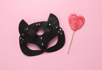 BDSM leather cat mask with lollipop on a pink background. Top view. flat lay