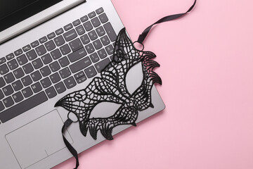 Online erotic chat. Lace cat mask with laptop on a pink background. Top view. flat lay