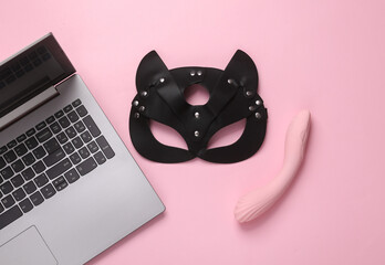 Online erotic chat. BDSM leather cat mask with vibrator and laptop on a pink background. Top view. flat lay