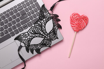 Online erotic chat. Lace cat mask with laptop and lollipop on a pink background. Top view. flat lay