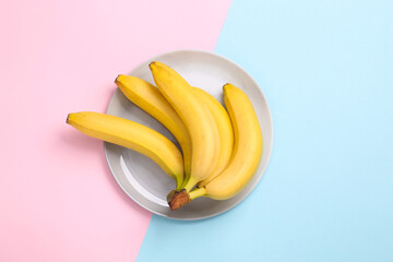 Ripe yellow bananas on plate, blue-pink pastel background. Top view