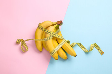 Bananas wrapped with measuring tape on blue-pink pastel background. Healthy food concept. Top view