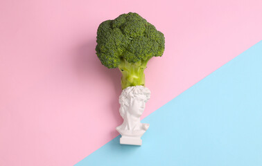 Healthy food concept. David bust with broccoli on pink blue background. Top view