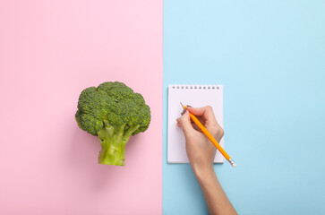 Diet plan. Broccoli, hand write on notepad on blue pink pastel background. Top view. Flat lay