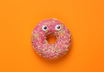 Minimal food concept. Donut with eyes on Orange background. Halloween still life