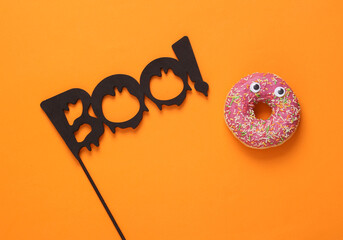 Halloween minimal still life. Word boo and donut with eyes on orange background