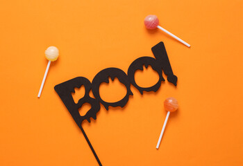 Halloween minimal still life. Word boo with lollipops on orange background