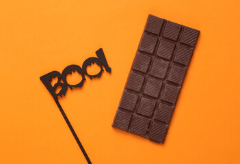 Halloween minimal still life. The word boo on a stick with a bar of chocolate on an orange background