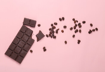Broken bar of chocolate with coffee beans on a pink background. Top view