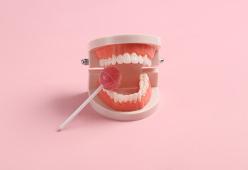 Human jaw model nibbles on a lollipop on a pink background. Minimal still life