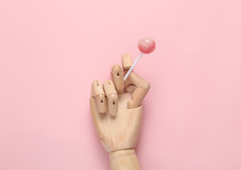 Obraz premium Wooden hand with lollipop on pink background
