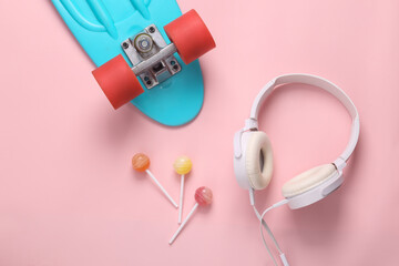 Youth hipster still life. Penny board with headphones and lollipops on a pink background. Top view....
