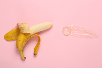 Sex education. Ripe banana with condom on pink background