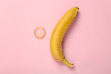 Sex education. Ripe banana with condom on pink background