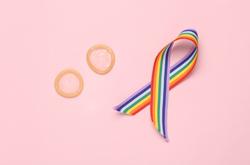 Two condoms with lgbt rainbow ribbon on a pink background.