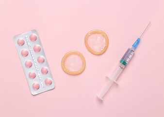 Contraceptives. Condoms with birth control pills and a syringe on a pink background.