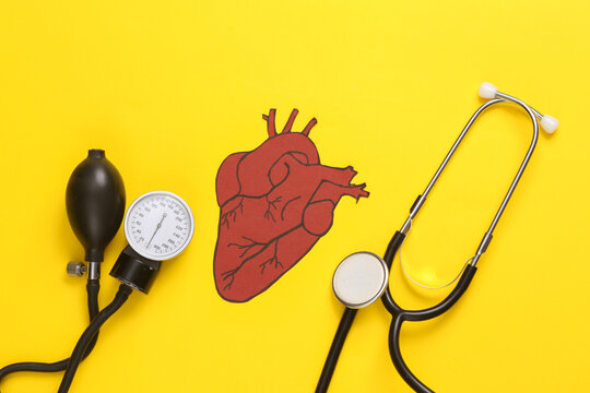 Diagnosis of cardiovascular diseases. Medical monometer with stethoscope and anatomical heart on a yellow background. Flat lay