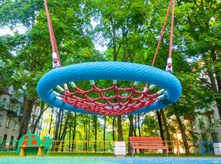 Round swing seat made of mesh in playground. Empty blue rope web nest for swinging closeup.