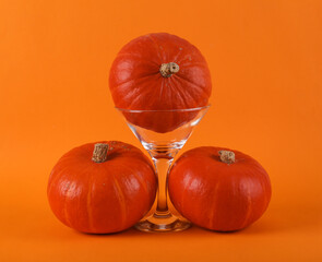 Minimal halloween still life. Cocktail glass with pumpkins on orange background