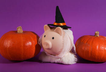 A piggy bank with a witch's hat and wrapped in bandages and pumpkins on a purple background. Trick...