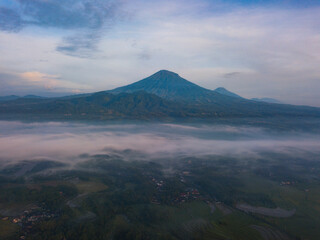 Fototapeta premium Drone photo of Mount Sumbing with sea of fog covered the land of plantation and trees in the morning. Central Java, Indonesia