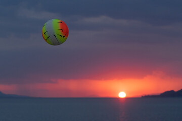 Beach volleyball in the air while playing against a vivd sunset.
