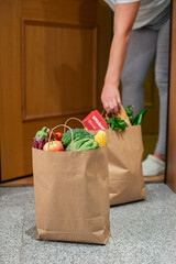 A woman picks up a bag of food at the door of her house. Coronavirus. Quarantine. Stay at home, Online shopping. Vegetables and fruits delivery during quarantine and self-isolation