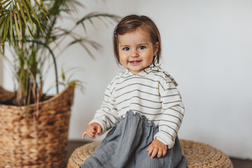 Pretty one year toddler girl in grey and white stripped dress posing in eco studio. Copy space.