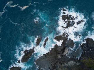 Overhead drone photo of corral rock hit by the sea wave. The sea water looks blue and made white...
