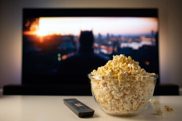 A glass bowl of popcorn and remote control in the background the TV works. Evening cozy watching a...