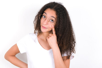 young beautiful girl with afro hairstyle wearing white t-shirt over white wall, looking, observing,...