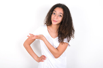 young beautiful girl with afro hairstyle wearing white t-shirt over white wall says: wow how exciting it is, has amazed expression, shows something on blank space with palm. Advertisement concept.