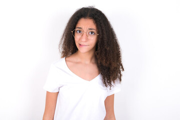 Fototapeta premium young beautiful girl with afro hairstyle wearing white t-shirt over white wall being nervous and scared biting lips looking camera with impatient expression, pensive.