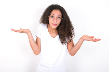 Puzzled and clueless young beautiful girl with afro hairstyle wearing white t-shirt over white wall...