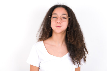 young beautiful girl with afro hairstyle wearing white t-shirt over white wall puffing cheeks with...