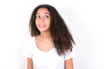 Oops! Portrait of young beautiful girl with afro hairstyle wearing white t-shirt over white wall  clenches teeth and looks confusedly aside, realizes her bad mistake,