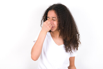 Very upset, young beautiful girl with afro hairstyle wearing white t-shirt over white wall touching nose between closed eyes, wants to cry, having stressful relationship or having troubles with work