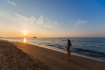 young beauty girl at beach near sea poses against the backdrop of the sunset. stylish swimsuit and boater