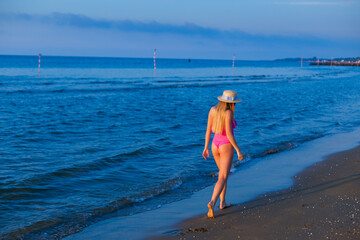 back beautiful slim girl with long hair on the background of the sea and horizon. pink swimsuit and boater