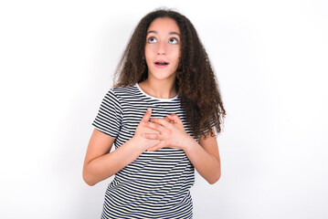 Happy smiling young beautiful girl with afro hairstyle wearing striped t-shirt over white wall has hands on chest near heart. Human emotions, real feelings and facial expression concept.