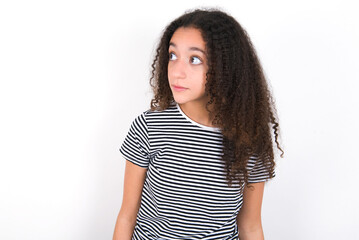 young beautiful girl with afro hairstyle wearing striped t-shirt over white wall stares aside with wondered expression has speechless expression. Embarrassed model looks in surprise