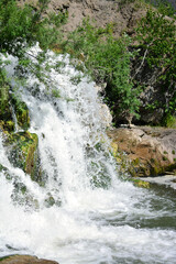 Small waterfall surrounded by mossy rocks, horizontal photo summer day with tree branches