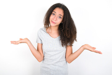 Careless attractive young beautiful girl with afro hairstyle wearing grey t-shirt over white wall shrugging shoulders, oops.