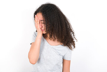 young beautiful girl with afro hairstyle wearing grey t-shirt over white wall with sad expression covering face with hands while crying. Depression concept.